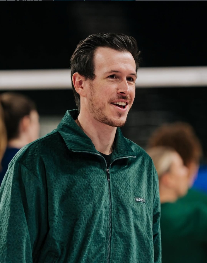 Remi Pourrat coaching courtside in a volleyball gym.